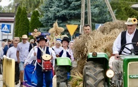 Korow&oacute;d dożynkowy przed kt&oacute;rym jadą ciągniki z przyczepą pełną siana