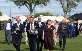 Korow&oacute;d dożynkowy na kt&oacute;rym widać starost&oacute;w dożynkowych, włodarzy gminy, radnych oraz proboszcza