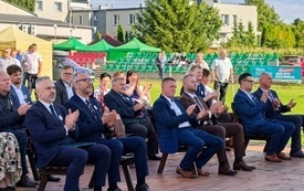 Włodarze gminy, sołtysi, radni siedzący na ławkach i bijący brawa