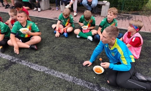 Grupka dzieci siedzących na murawie, spożywająca zupę